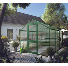 Grünes Gewächshaus mit Satteldach und Hohlkammerplatten in einem hellen Garten neben einem Wohnhaus.