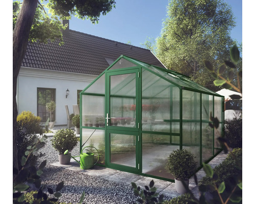 Grünes Gewächshaus mit Satteldach und Hohlkammerplatten in einem hellen Garten neben einem Wohnhaus.