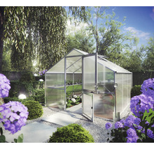 Gewächshaus aus Aluminium mit Hohlkammerplatten und geteilter Tür, freistehend in einem bepflanzten Garten mit Schaufel und Kiesweg.