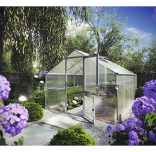 Gewächshaus aus Aluminium und Polykarbonat mit geteilter Tür in einem hellen Garten mit Blumen und Gehwegen.