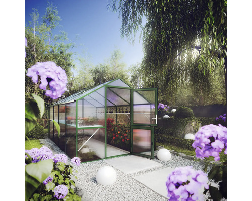 Gewächshaus mit grünem Rahmen und transparenten Hohlkammerplatten in einem hellen Garten mit Pflanzen, Kies und lila Blumen.