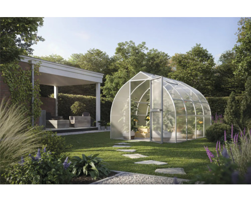 Modernes bogenförmiges Gewächshaus mit lichtdurchlässigen Paneelen in einem weitläufigen Garten mit Rasen, Steinpfad und Außenterrasse.
