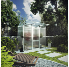 Modernes Gewächshaus aus Aluminium und Glas in einem hellen Garten mit Gabionenwand, Rasen und Steinplatten.