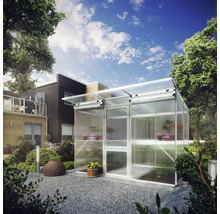 Modernes Gewächshaus aus Aluminium und Polycarbonat in einem gestalteten Garten mit Kies und Pflanzen vor einem Wohnhaus.