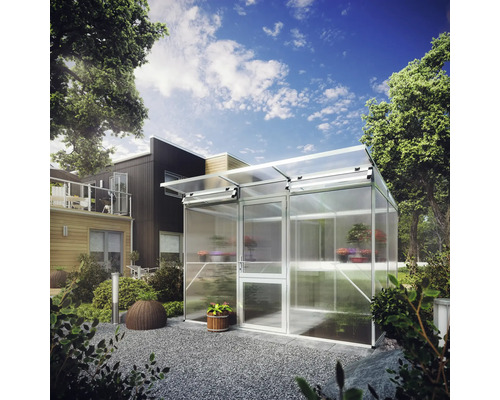 Modernes Gewächshaus aus Aluminium und Polycarbonat in einem gestalteten Garten mit Kies und Pflanzen vor einem Wohnhaus.
