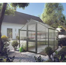 Freistehendes Gewächshaus mit anthrazitfarbenem Aluminiumrahmen und Hohlkammerplatten in einem hellen Garten neben einem Wohnhaus.