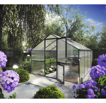 Modernes Gewächshaus mit dunklem Metallrahmen und Hohlkammerplatten in einem hellen Garten mit Hortensien und einem Kiesweg.