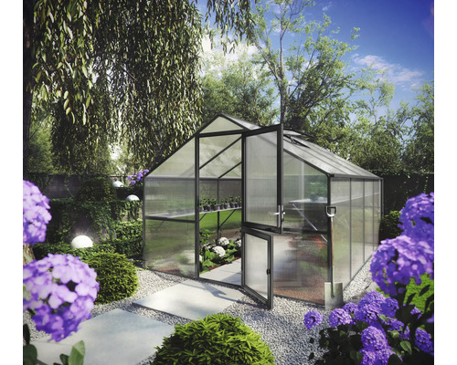 Modernes Gewächshaus mit dunklem Metallrahmen und Hohlkammerplatten in einem hellen Garten mit Hortensien und einem Kiesweg.