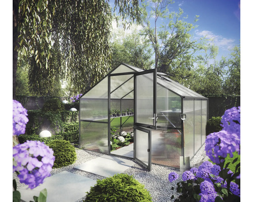 Freistehendes Gewächshaus mit grauem Rahmen und Doppelstegplatten in einem hellen Garten mit Kiesweg und violetten Blumen.