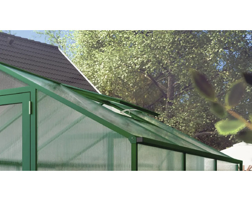 Gewächshaus mit grünem Aluminiumrahmen und Hohlkammerplatten, offenes Dachfenster zur Belüftung, im Garten neben Haus und Bäumen.