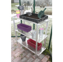 Dreistöckiges Aluminium-Gewächshausregal mit Gartenutensilien wie einer Pflanzschale mit Erde, einer Gießkanne und verschiedenen Pflanztöpfen.