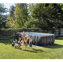 Rechteckiges dunkelgraues Aufstellbecken mit Metallrahmen in hellem Garten. Eine Familie steht daneben auf dem Rasen.