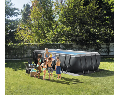 Rechteckiges dunkelgraues Aufstellbecken mit Metallrahmen in hellem Garten. Eine Familie steht daneben auf dem Rasen.
