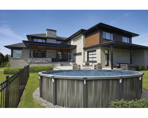 Moderner Garten mit rundem Aufstellpool in Holzoptik, auf einer Rasenfläche neben einem Haus aus Stein mit Terrasse und Gartenmöbeln.