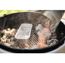 Glühende Grillbriketts werden aus einem Anzündkamin in einen Holzkohlegrill neben eine Aluminium-Tropfschale mit Weber Logo gefüllt.