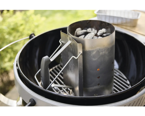 Anzündkamin aus Metall gefüllt mit Grillkohle auf einem Grillrost in einem Kugelgrill im Freien.