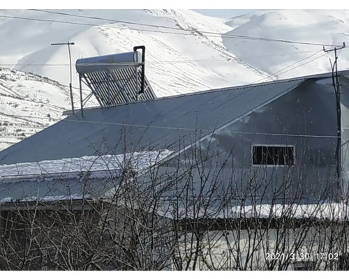 Solarthermie-Anlage mit Vakuumröhren und Speicher auf einem Metalldach in einer winterlichen Berglandschaft.