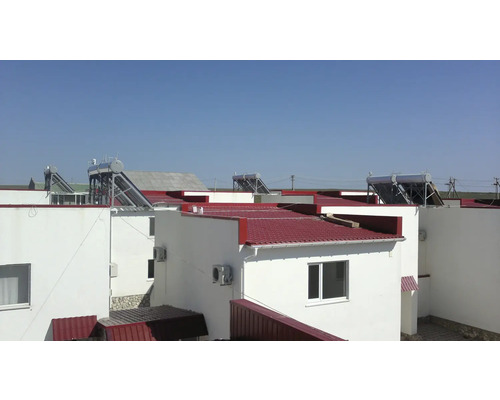 Weiße Wohnhäuser mit roten Dächern und darauf installierten Solarthermie-Anlagen mit Vakuumröhrenkollektoren und Warmwasserspeichern.