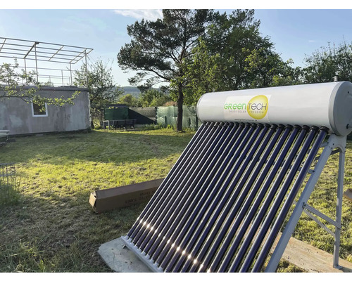 Green Tech Logo auf einer Solarthermieanlage mit Vakuumröhren und Warmwasserspeicher auf einem Metallgestell in einem hellen Garten.