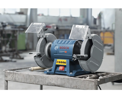 Bosch Professional Doppelschleifmaschine mit zwei Schleifscheiben und Funkenschutz auf einem Metalltisch in einer organisierten Werkstatt.