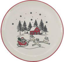 Runder Keramikteller mit rotem Rand und weihnachtlichem Motiv: Weihnachtsmann im Schlitten mit Rentieren, Haus und Tannen im Schnee.