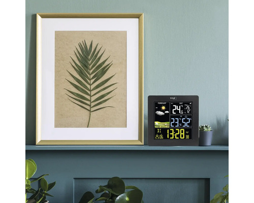 Digitale Funk-Wetterstation mit Farbdisplay, Anzeige von Uhrzeit, Innen- und Außentemperatur sowie Wettervorhersage, auf einem Regal im modernen Raum.