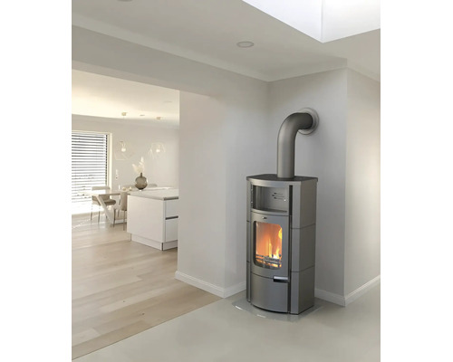 Moderner grauer Kaminofen mit brennendem Feuer in einem hellen, minimalistischen Raum mit Holzboden und offener Küche.