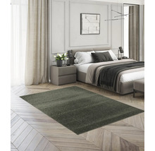 Ein rechteckiger, dunkelgrauer Hochflor-Teppich in einem modern eingerichteten Schlafzimmer auf hellem Parkettboden.