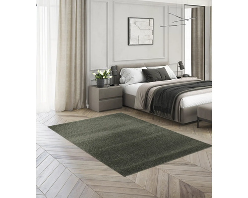 Ein rechteckiger, dunkelgrauer Hochflor-Teppich in einem modern eingerichteten Schlafzimmer auf hellem Parkettboden.