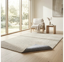 Hochflor-Teppich in einem hellen Wohnzimmer mit Holzfußboden und Sessel. Eine Ecke des Teppichs ist umgeschlagen.