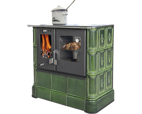 Holzherd mit grüner Kachelverkleidung, Brennkammer mit Feuer, Backrohr mit Gebäck und Kochtopf auf der Kochfläche.