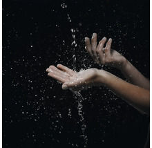Hände, in die ein Wasserstrahl fließt und Spritzer sowie Wassertropfen erzeugt.