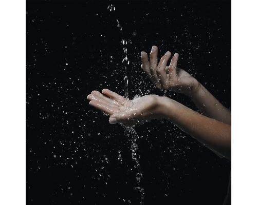Hände, in die ein Wasserstrahl fließt und Spritzer sowie Wassertropfen erzeugt.