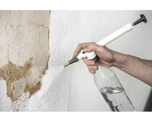 Eine Person besprüht eine Wand mit einem Drucksprüher, um Tapetenreste zu lösen.