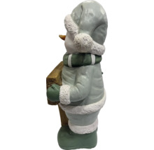 Schneemann-Figur aus Magnesia, hält einen Holzklotz, trägt Mütze, Schal und Handschuhe, Weihnachtsdekoration für draußen.