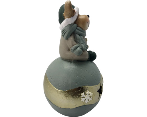Weihnachtsfigur kleiner Bär mit Mütze und Schal sitzend auf einer dekorativen Kugel mit Schneeflockenverzierung.