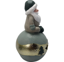Weihnachtsfigur Wichtel sitzend auf einer Kugel mit dekorativem Band und Tannenbaum-Aussparung.