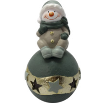Schneemann-Figur sitzend auf einer Dekokugel mit Sternen, Weihnachtsdekoration aus Keramik.