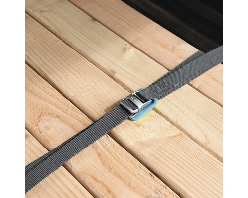 Grauer Spanngurt mit Metallschnalle sichert mehrere Holzbretter.
