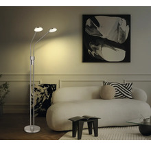 Zweiflammige LED-Stehleuchte aus Metall in einem hellen Wohnzimmer mit weißem Sofa und abstrakten Bildern.