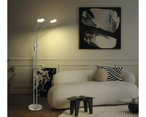 Zweiflammige LED-Stehleuchte aus Metall in einem hellen Wohnzimmer mit weißem Sofa und abstrakten Bildern.