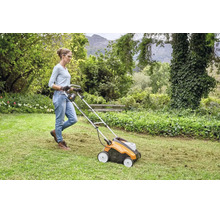 Frau bedient einen Vertikutierer auf einer Rasenfläche in einem Garten.
