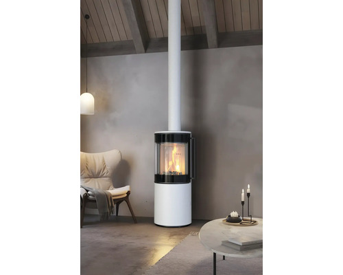 Moderner, runder Kaminofen in Weiß mit brennendem Feuer im Wohnzimmer neben einem Sessel und einem Tisch.