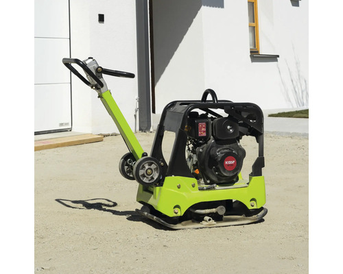 Rüttelplatte mit KOOP-Motor auf sandigem Boden vor einem Haus.