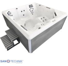 Quadratischer Außenwhirlpool mit Massagedüsen, Kopfstützen und grauer Treppe. Weiße Wanne und graue Verkleidung in Holzoptik.