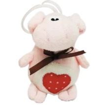 Plüsch-Schwein als Anhänger mit einer braunen Schleife und einem roten Herz mit weißen Punkten auf dem Bauch.