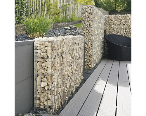 Gabionenwand aus Metallkörben mit hellen Steinen auf einer Terrasse mit grauen Dielen und Sichtschutzelementen im Garten.