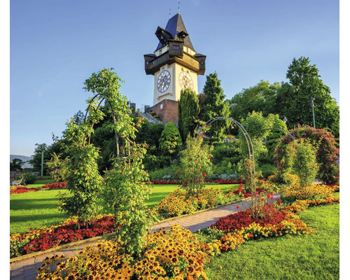 Fototapete mit dem Grazer Uhrturm über einer Parkanlage mit Blumenbeeten und Rankbögen.