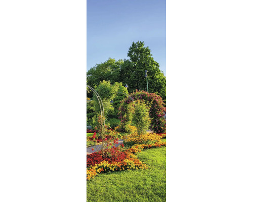 Hell gestalteter Garten mit einem Metall-Rosenbogen über einem Weg, bunten Blumenbeeten und hohen Bäumen.
