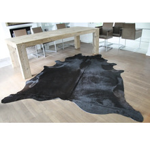 Ein schwarzes Kuhfell auf hellem Parkett in einem hellen, modernen Esszimmer mit großem Holztisch.